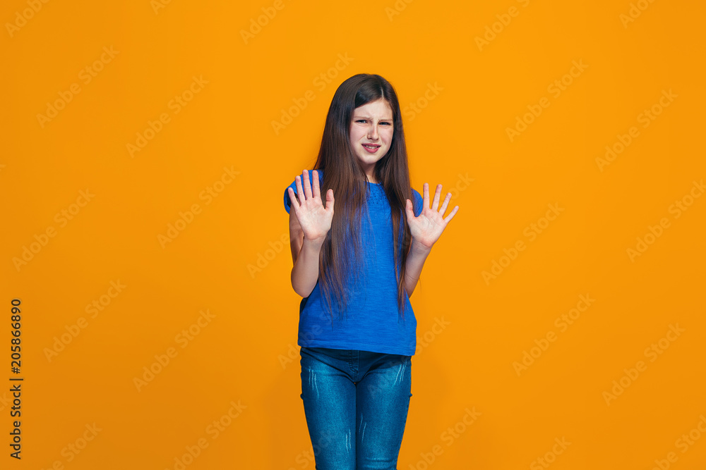 Doubtful pensive teen girl rejecting something against orange background Doubtful pensive teen girl rejecting something against orange background