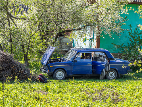Blue old car at the countryside under the tree near the house