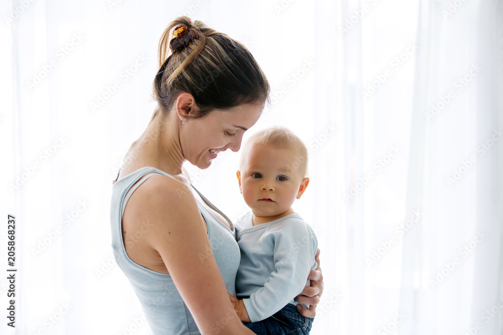 Young mother, embracing with tenderness and care her baby boy, smiling happilye Young mother, embracing with tenderness and care her baby boy, smiling happilye