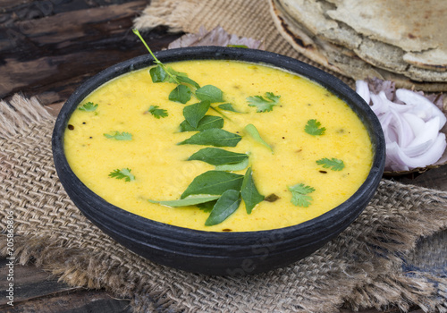 Rajasthani And Gujarati Traditional Cuisine Kadhi or Bajra Roti with Fried Chili, Onion or Lemon - Indian Vegetarian Curry Made of Buttermilk And Chick Pea Flour. Cuisine on Vintage Wooden Background photo