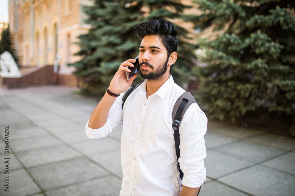 Handsome young Indian student talking smartphone in the city street Handsome young Indian student talking smartphone in the city street