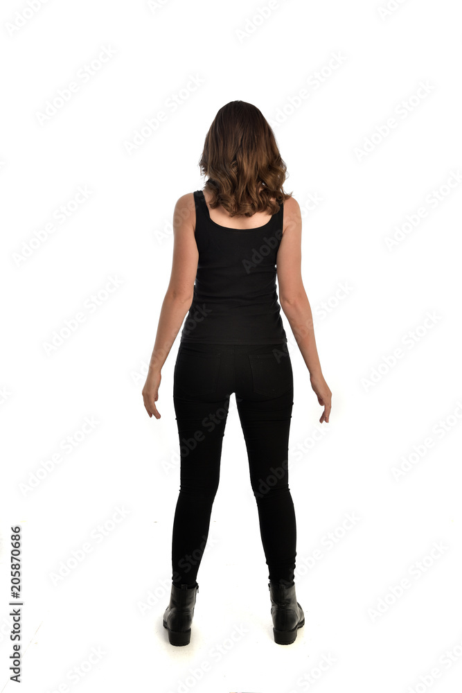 Fototapeta premium full length portrait of brunette girl wearing black singlet, jeans jeans and boots. standing pose, with back view. isolated on white studio background.
