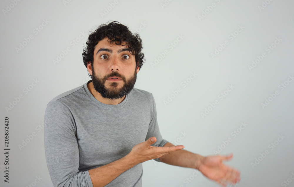 Handsome bruHandsome brunette man with beard and curly hair surprised shnette man with beard and curly hair astonished showing direction and pointing with finger. Studio portrait over gray background. Handsome bruHandsome brunette man with beard and curly hair surprised shnette man with beard and curly hair astonished showing direction and pointing with finger. Studio portrait over gray background.