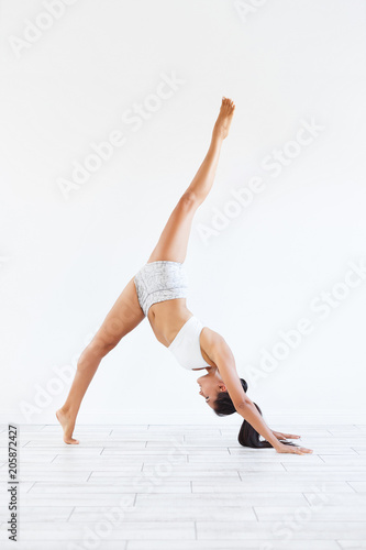 Beautiful young woman in gymnastic costume fitness instructor doing Urdhva Prasarita Ekapadasana exercise on white background. Copyspace