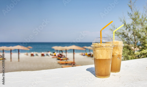 Fototapeta Naklejka Na Ścianę i Meble -  Glass of ice coffee on white wooden table and tropical beach and blue sea and clear sky background.