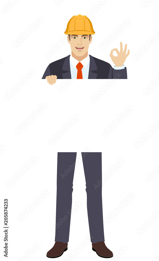OK! Businessman in construction helmet holding white blank poster and showing a okay hand sign