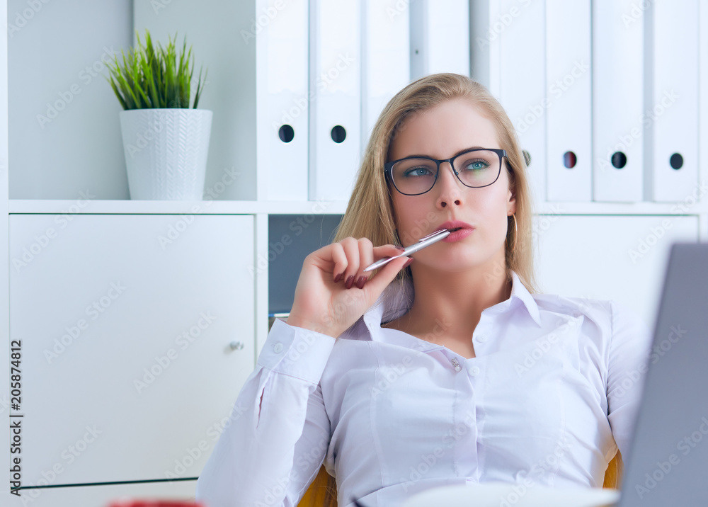 Young Caucasian business woman in glasses looks thoughtfully into the distance holding the pen in her mouth and thinks.