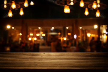 Image of wooden table in front of abstract blurred restaurant lights background.