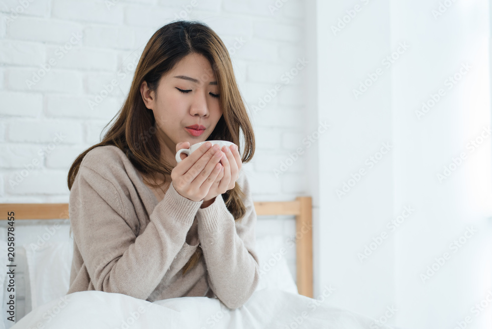 Beautiful Asian woman enjoying warm coffee on bed in her bedroom. Relaxation in bed. Beautiful Asian female wearing comfortable sweater holding a cup of coffee. lifestyle Asian woman at home concept. Beautiful Asian woman enjoying warm coffee on bed in her bedroom. Relaxation in bed. Beautiful Asian female wearing comfortable sweater holding a cup of coffee. lifestyle Asian woman at home concept.