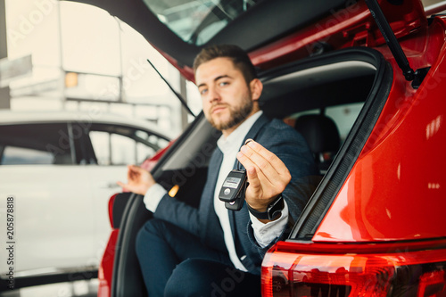 Excited businessman sitting in car. Showing new car key.