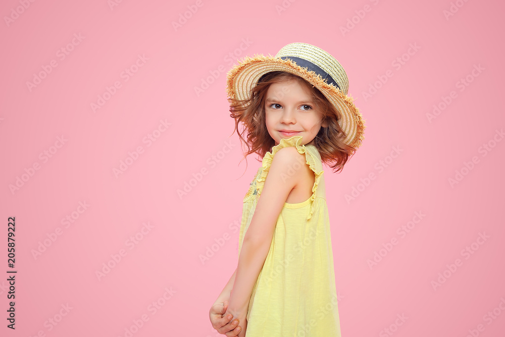 Close up portrait of a Beautiful girl in yellow dress and straw hat. Pretty tenderness kid looking away, posing on a pink studio background. Close up portrait of a Beautiful girl in yellow dress and straw hat. Pretty tenderness kid looking away, posing on a pink studio background.