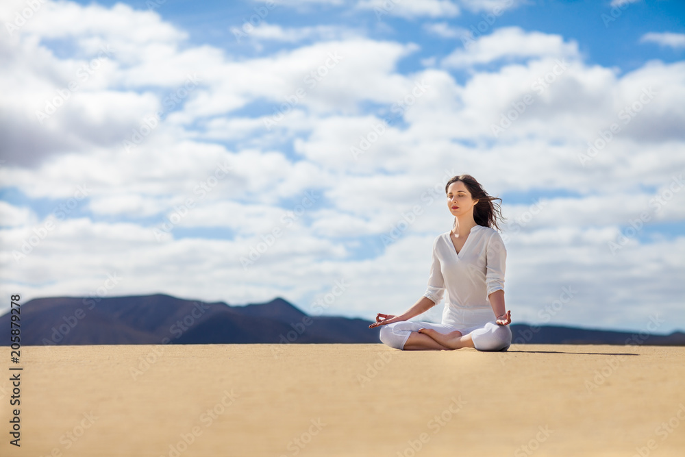Young woman meditating in Lotus Pose in desert on Canary Islands, Spain.