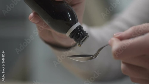 Woman pouring cough syrup into spoon, flu epidemic, herbal remedies, closeup photo