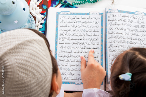 Muslim brother and sister pointing to the word : Ramadan (The holy Month) while reading the Quran in a mosque photo