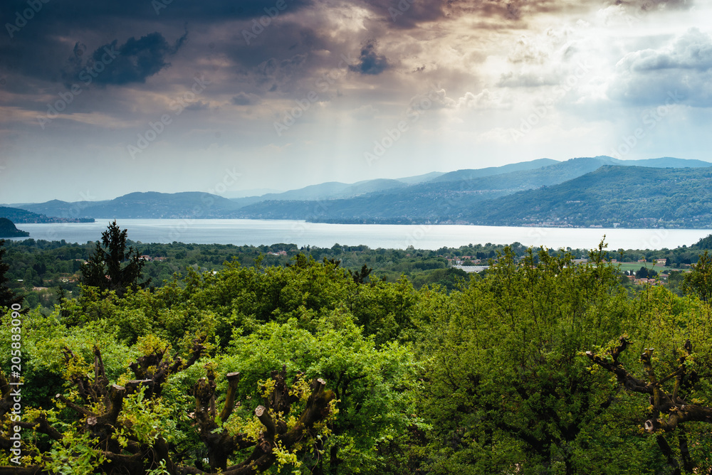panorama of Lake Maggiore green woods around and cloudy sky with rays of light, storm approaching