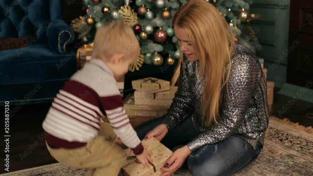 A little boy gives a gift to his mother on Christmas night near a large decorated Christmas tree. Christmas. Family. New year. A little boy gives a gift to his mother on Christmas night near a large decorated Christmas tree. Christmas. Family. New year.