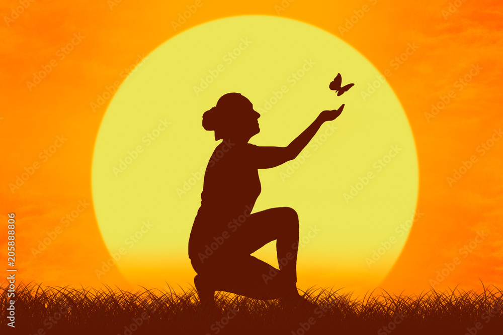 Silhouette of a girl with butterfly flying from her hands against the setting sun.