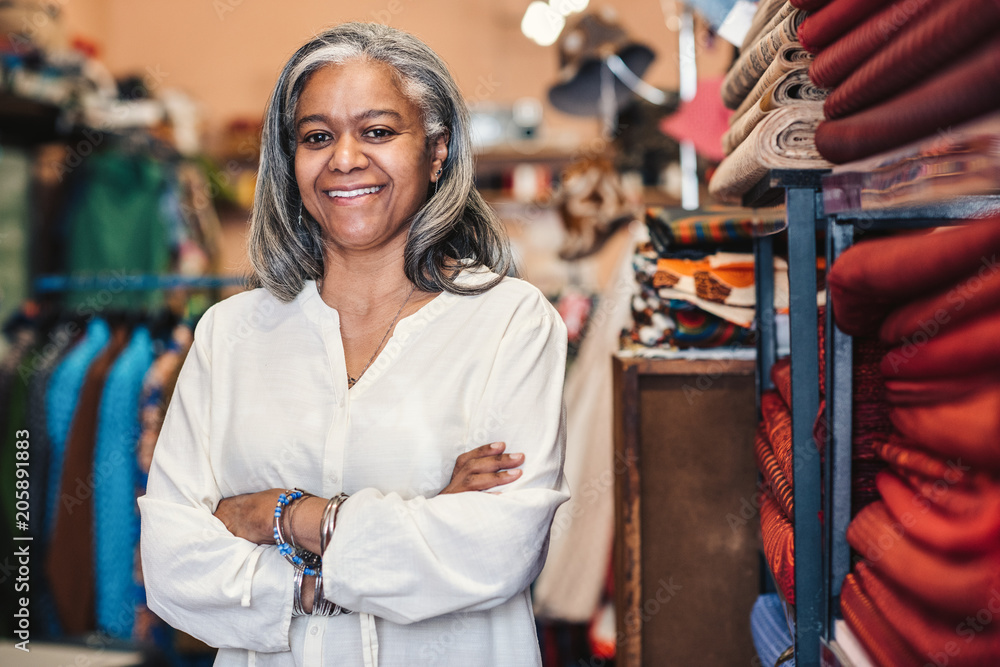 Smiling mature woman standing in her colorful fabric shop