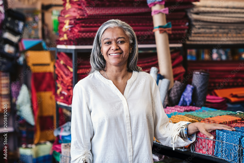 Smiling mature woman standing by cloth in her fabric store