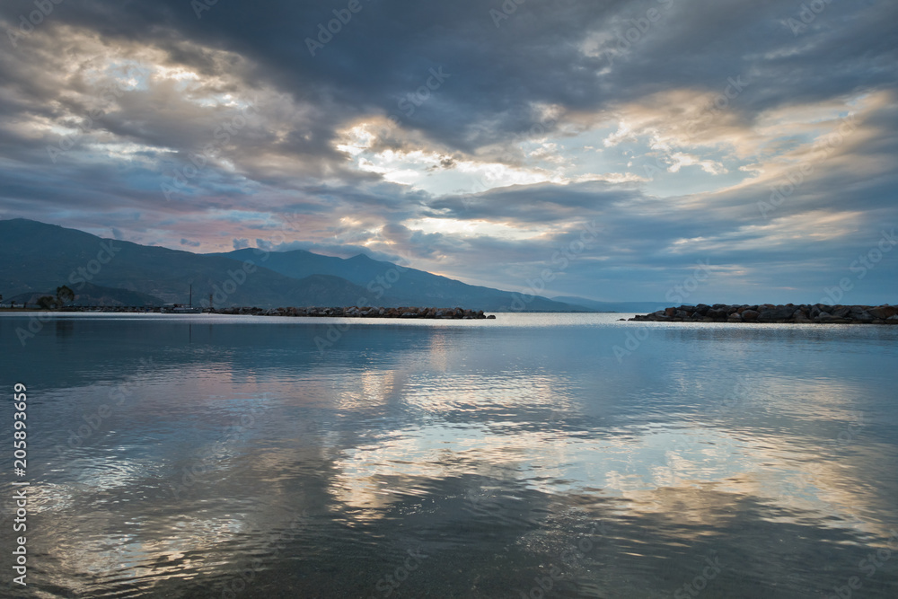 Cloud reflections in a water of aegean sea at sunrise, Volos harbor with Pelion mountain in background, Greece