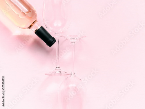 Bottle of pink wine and two glasses of wine on a soft light pink wood table, mock up. Flat lay, top view, copy space