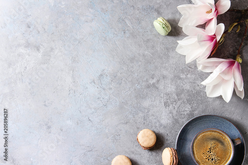 Blue cup of black espresso coffee, french dessert macaroons and spring flowers magnolia branches over grey texture background. Top view, space. Spring greeting card, wallpapers