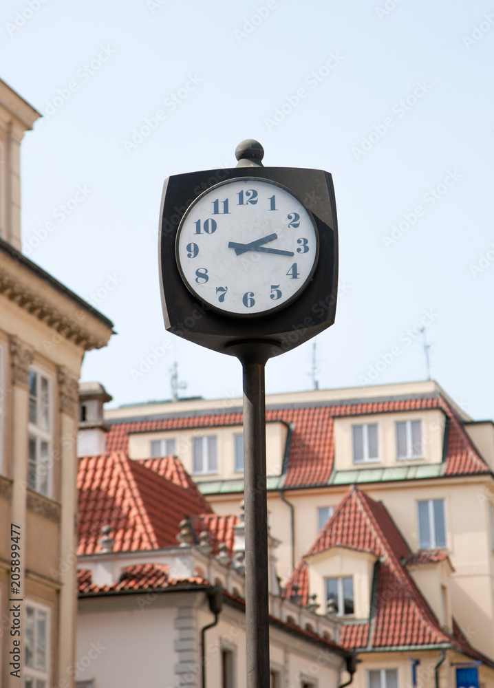 Street clock. In the background of the house with tiled roofs