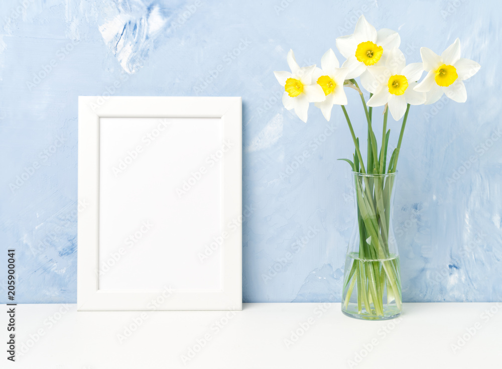 Bouquet of fresh flowers, white frame on table, opposite blue textured concrete wall. Empty space for text. Mock up. Bouquet of fresh flowers, white frame on table, opposite blue textured concrete wall. Empty space for text. Mock up.