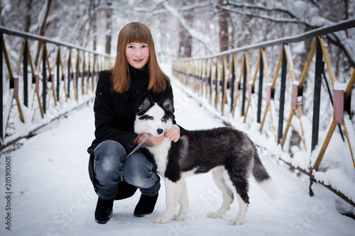 Young beautiful girl playing with siberian husky dog in the winter park