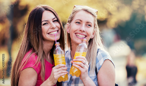 Two smiling girls drinking juice, having fun together in the city. Lifestyle concept