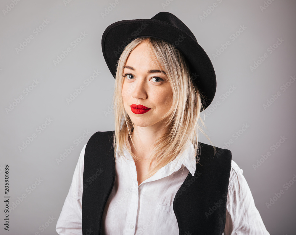 Blonde woman portrait in black hat. Red lipstick make up. Gray background