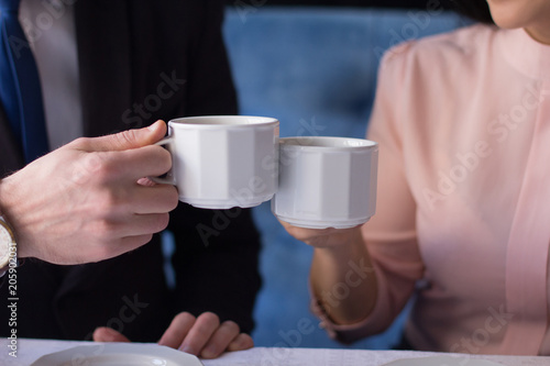 Close up of two partners clang cups of coffee after discussing agreement. Two partners working together and having coffee.