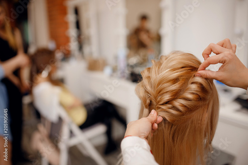 Woman hairdresser making hairstyle to blonde girl in beauty salon.