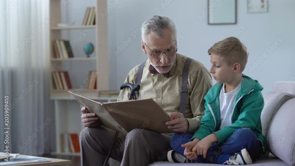 Old man reading book aloud to grandson, giving experience to younger generation Old man reading book aloud to grandson, giving experience to younger generation