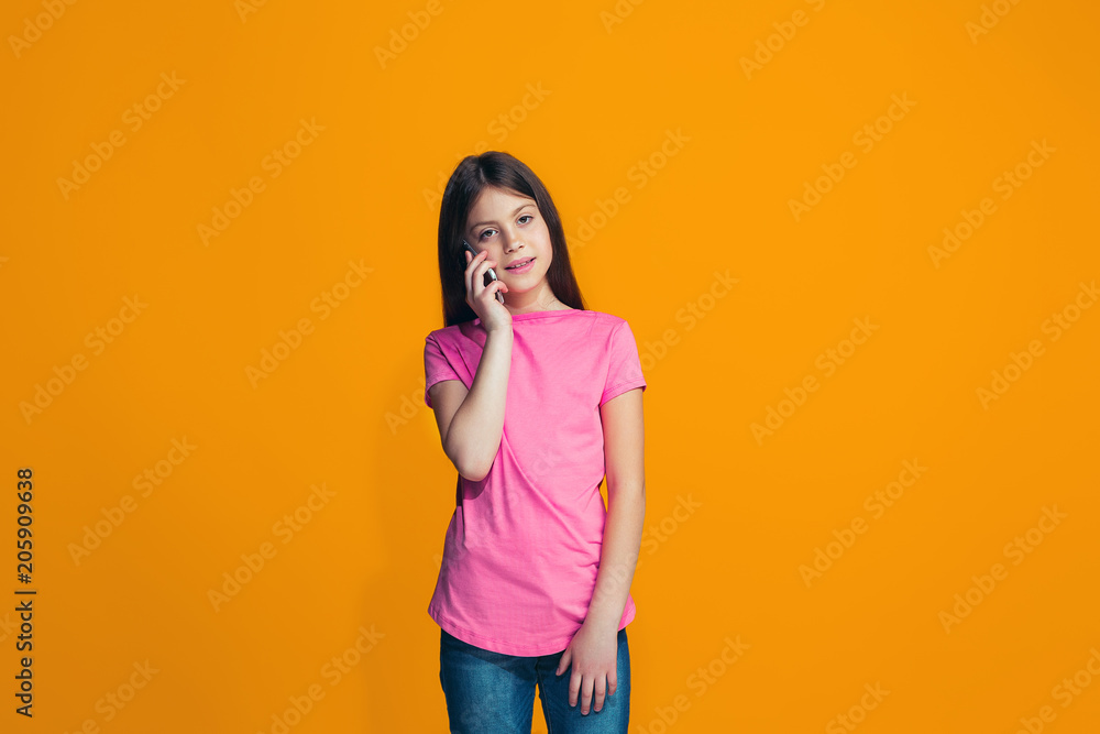 The happy teen girl standing and smiling against orange background. The happy teen girl standing and smiling against orange background.