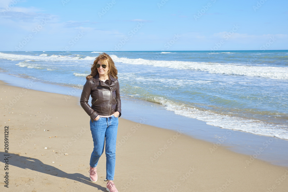 Woman standing at the beach in casual jeans and leather jacket