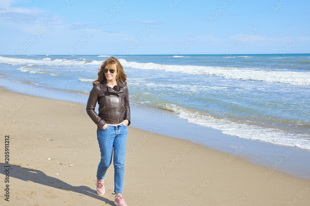 Woman standing at the beach in casual jeans and leather jacket Woman standing at the beach in casual jeans and leather jacket