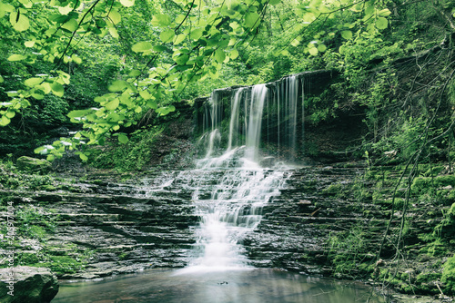 Beautiful mountain rainforest waterfall with fast flowing water and rocks  long exposure. Natural seasonal travel outdoor background in hipster vintage style