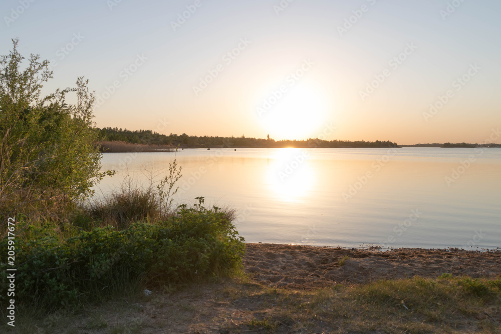 Summer sunset on a lake, calm water, orange sky, sun going down