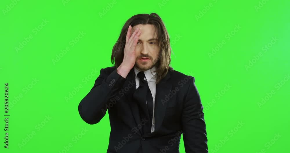 Portrait shot of the handsome young Caucasian man with long hair in the suit and tie looking very tired while standing on the green screen background. Chroma key Portrait shot of the handsome young Caucasian man with long hair in the suit and tie looking very tired while standing on the green screen background. Chroma key