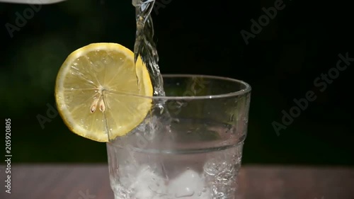 Pouring water with ice and lemon in glass, slow motion