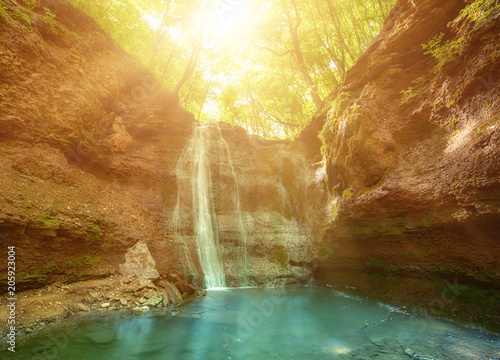 Beautiful mountain rainforest waterfall with fast flowing water and rocks, long exposure. Natural seasonal travel outdoor background with sun shihing photo