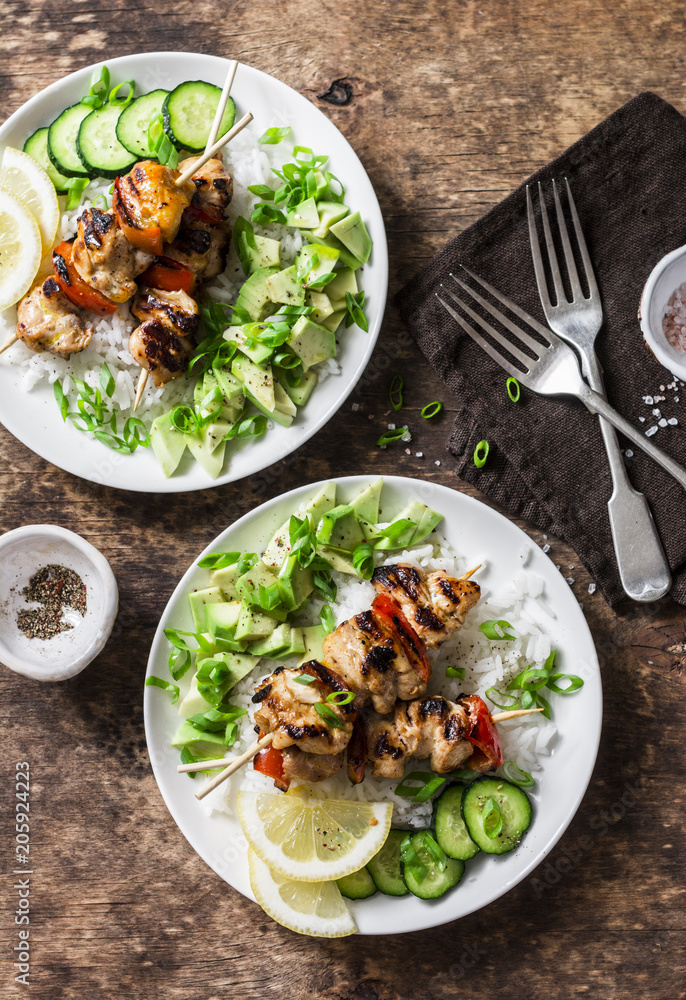 Grilled chili honey lime chicken skewers with rice and avocado salsa on wooden background, top view. Flat lay Grilled chili honey lime chicken skewers with rice and avocado salsa on wooden background, top view. Flat lay