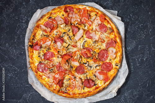 Fresh homemade pizza with pepperoni, ham, cheese and tomato sauce on rustic stone background