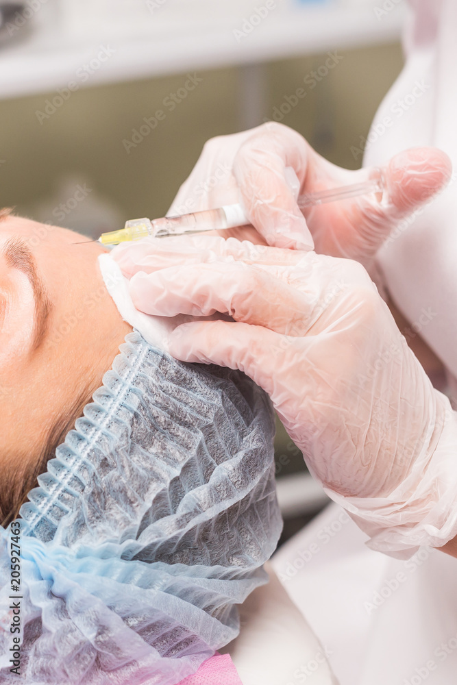 Close up of hands of young cosmetologist injecting in female face Close up of hands of young cosmetologist injecting in female face