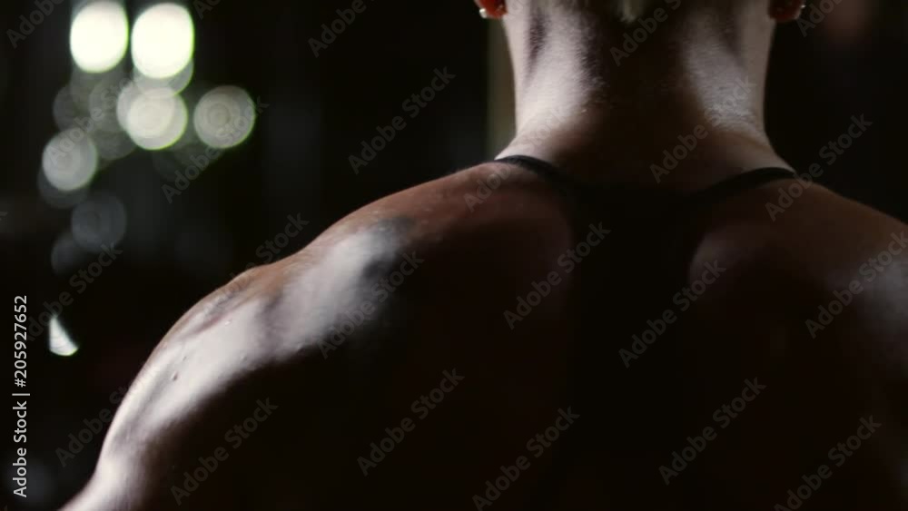 Rear view tracking shot of muscular shoulders of woman doing dumbbell lateral raises Rear view tracking shot of muscular shoulders of woman doing dumbbell lateral raises