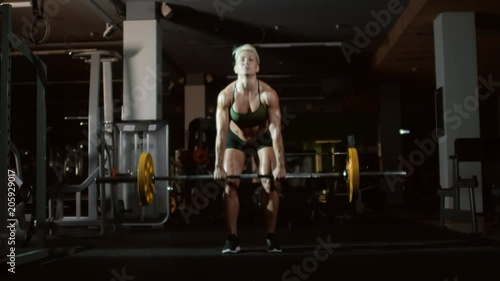 Full length of blonde woman in sports bra and shorts picking up barbell from the floor in gym and doing deadlift exercise photo