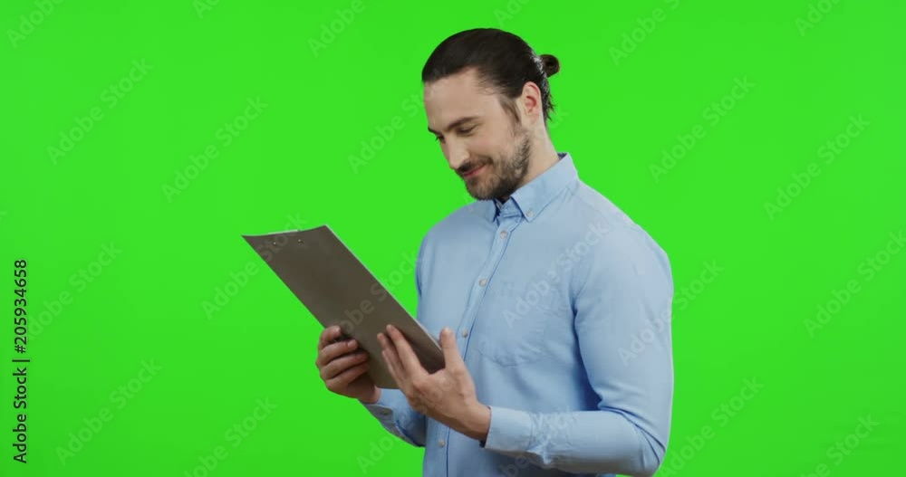 Portrait shot of the good looking Caucasian man in the blue shirt holding a folder with documents and looking at them with a smile. Green screen. Chroma key Portrait shot of the good looking Caucasian man in the blue shirt holding a folder with documents and looking at them with a smile. Green screen. Chroma key