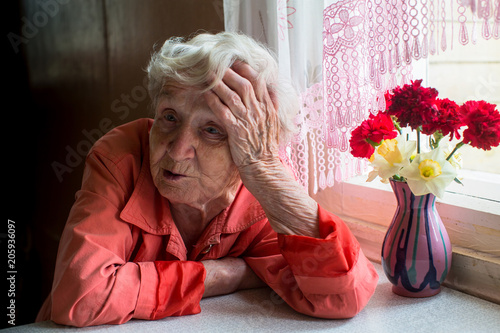 Elderly woman looks sadly sitting near the window.