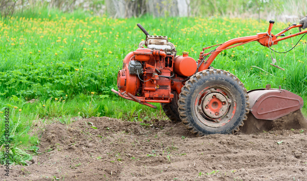 A small tractor, a motoblock, with a seed mill, working on the edge of a freshly-fallen and treated field, soil prepared for sowing. The concept of agriculture, agriculture and agricultural machinery. A small tractor, a motoblock, with a seed mill, working on the edge of a freshly-fallen and treated field, soil prepared for sowing. The concept of agriculture, agriculture and agricultural machinery.
